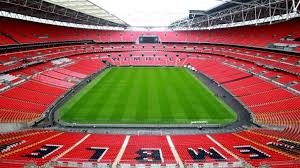 view of empty wembley stadium seating from inside stadium. rich green of pitch and bright red seats